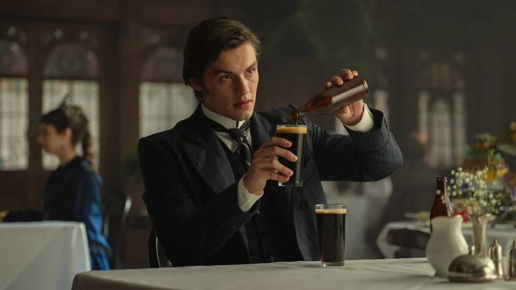 Louis Partridge stars in House of Guinness pouring a drink in a cup at a fancy dining table