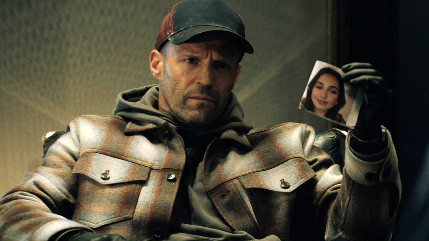 Jason Statham in A Working Man looking at a photo of a woman