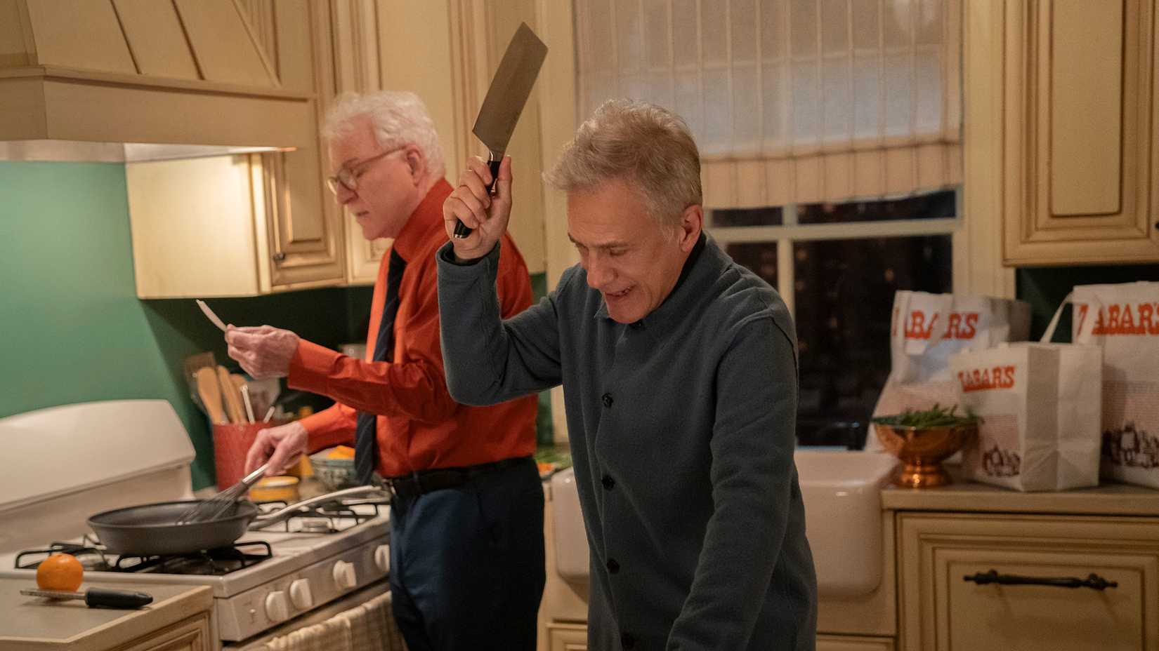 Sebastian with a meat cleaver in his hand while Charles cooks in the background in Only Murders in the Building.