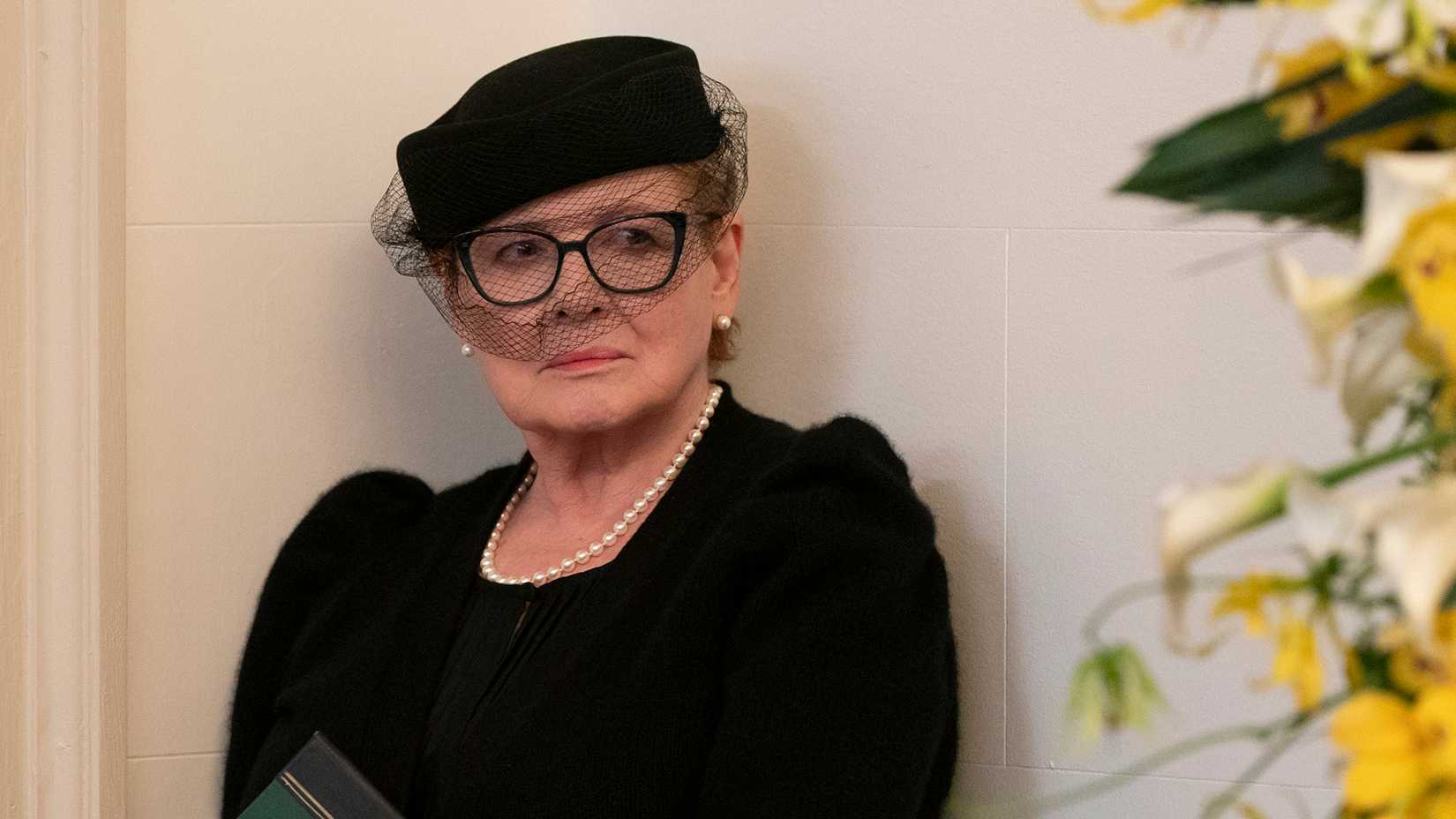 Ms. Coluca standing against a wall wearing all black in Only Murders in the Building.