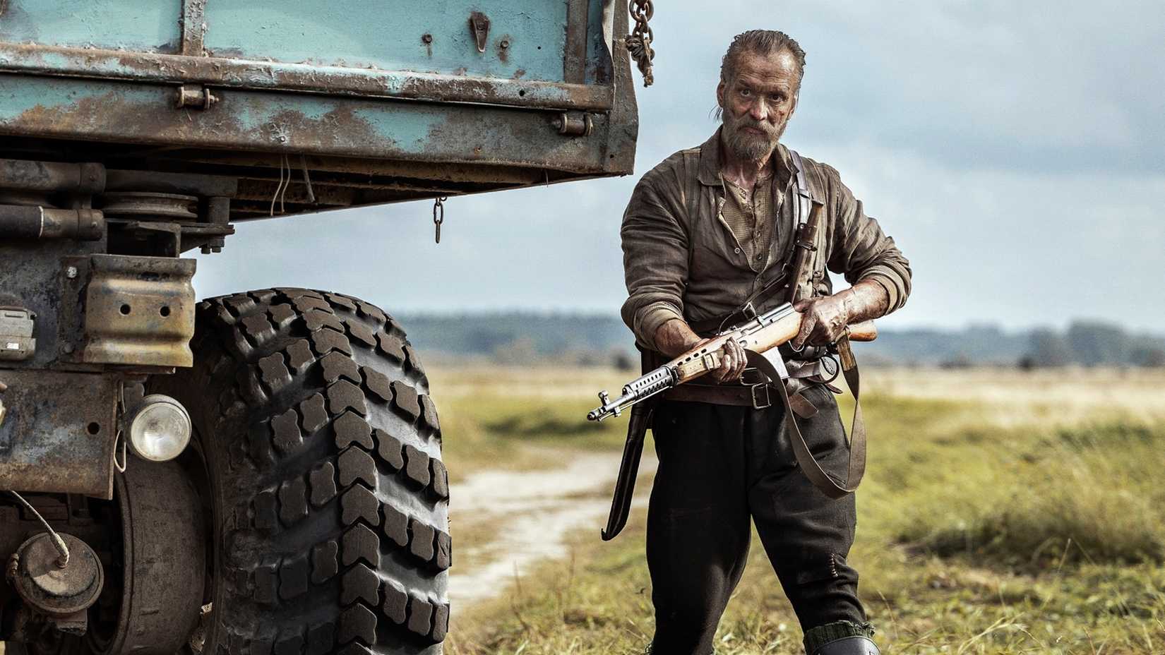 Jorma Tommila in Sisu: Road to Revenge holding a rifle next to a large truck