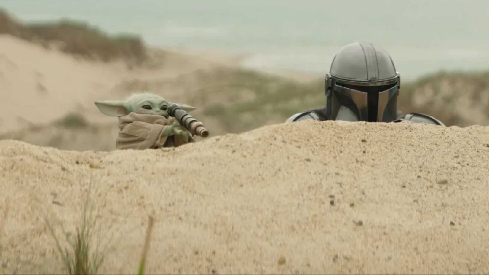 The Mandalorian & Grogu hiding behind some sand dunes
