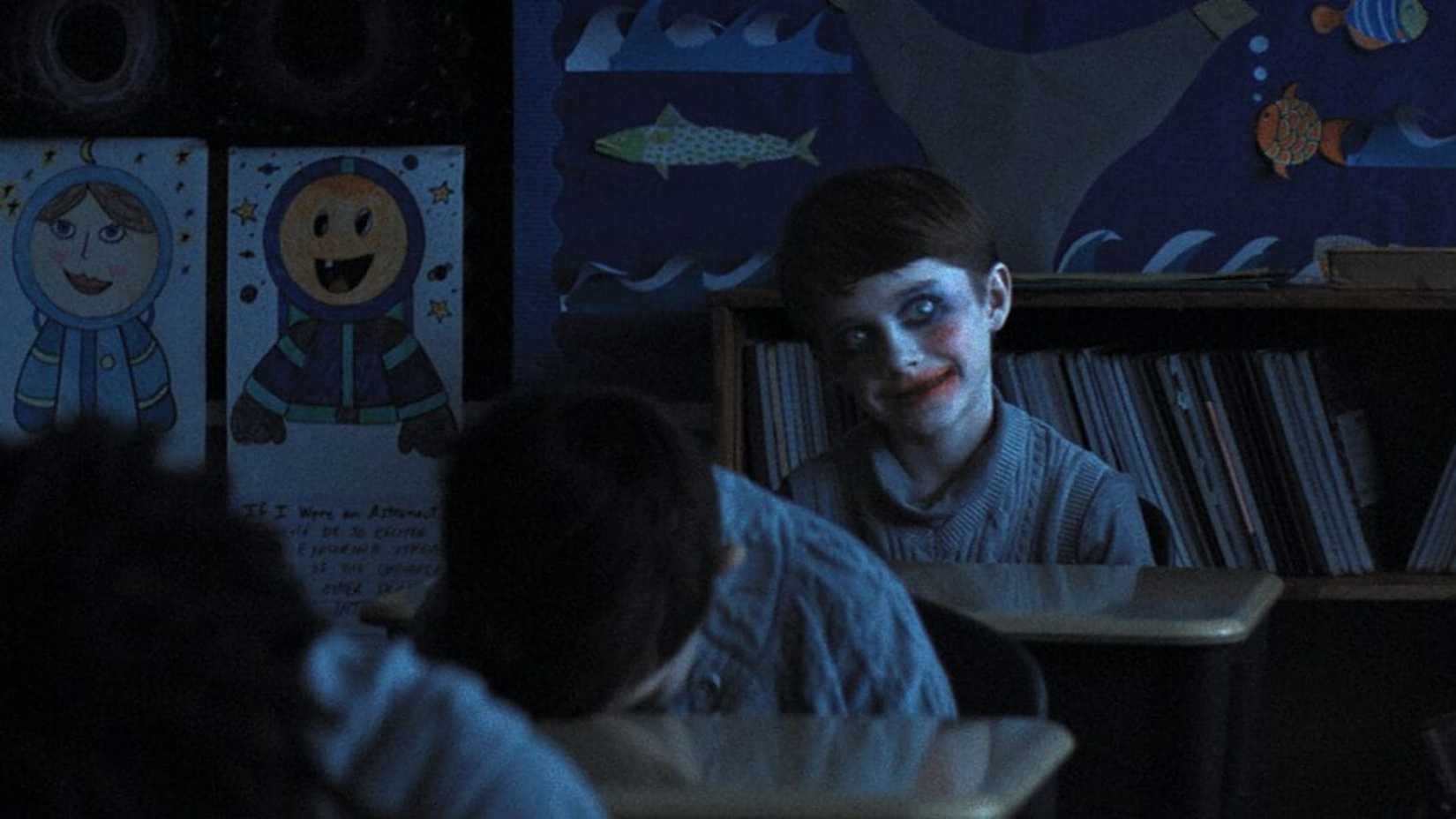 A child covered in makeup sits in a dark classroom in Weapons