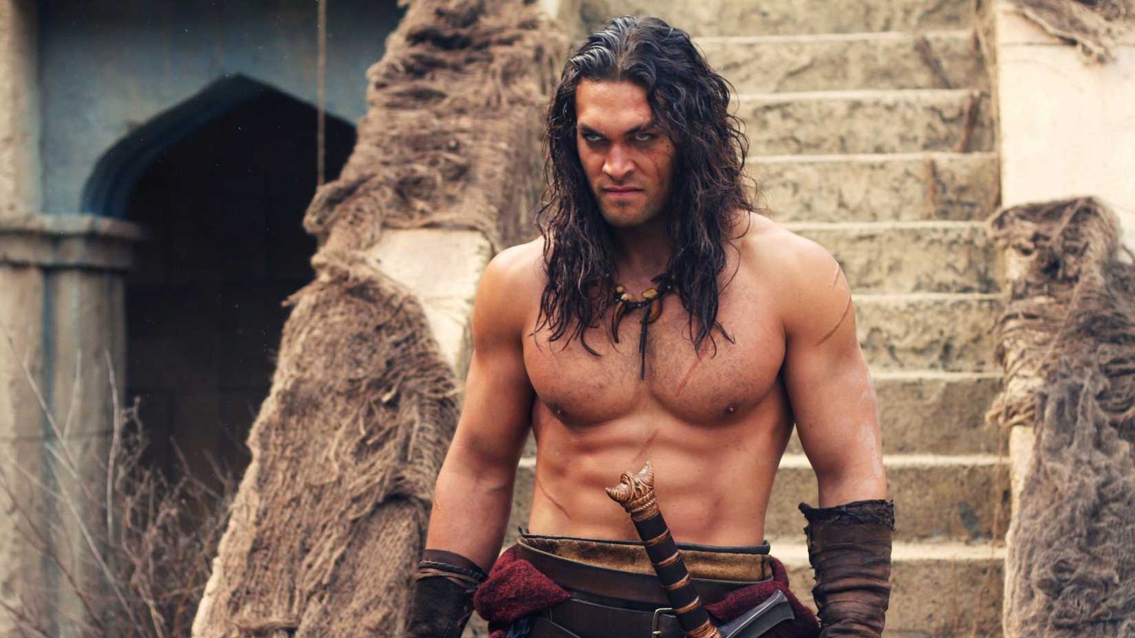 Jason Momoa as Conan in Conan the Barbarian with his shirt off and sword sheathed