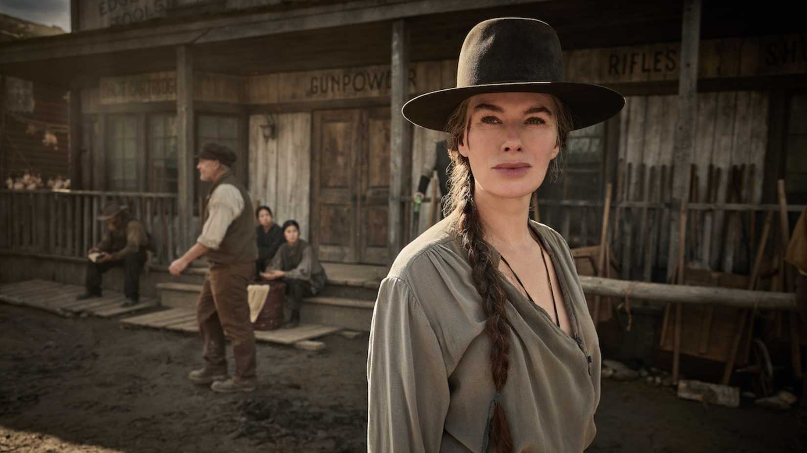 Lena Headey in The Abandons wearing a black hat and grey shirt standing outside of an old west store