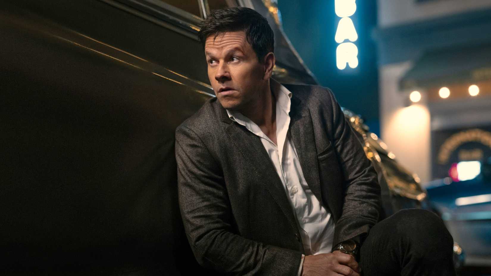 Mark Wahlberg in Play Dirty leaning against a car in a suit