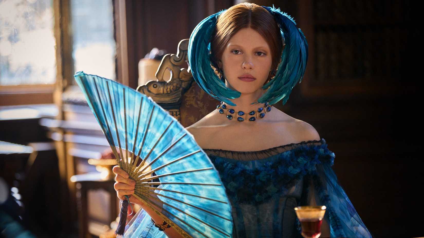Mia Goth as Lady Elizabeth Harlander in Frankenstein dressed in fancy clothes holding a fan