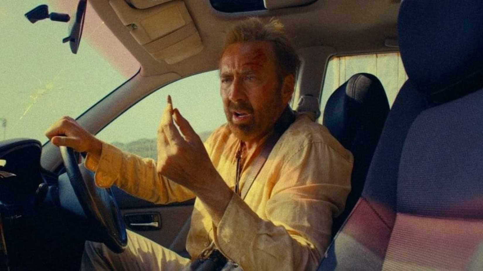 Nicolas Cage stares at a small item in the car in The Surfer