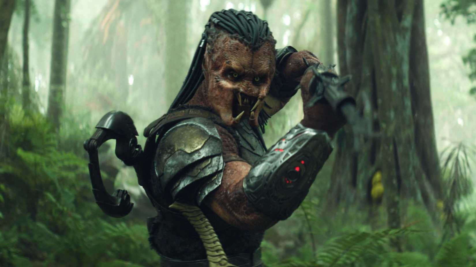 a Predator in Predator: Badlands standing in the forest with a weapons