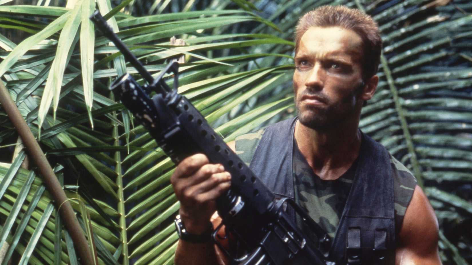 Arnold Schwarzenegger in Predator holding an assault rifle in the jungle wearing facepaint