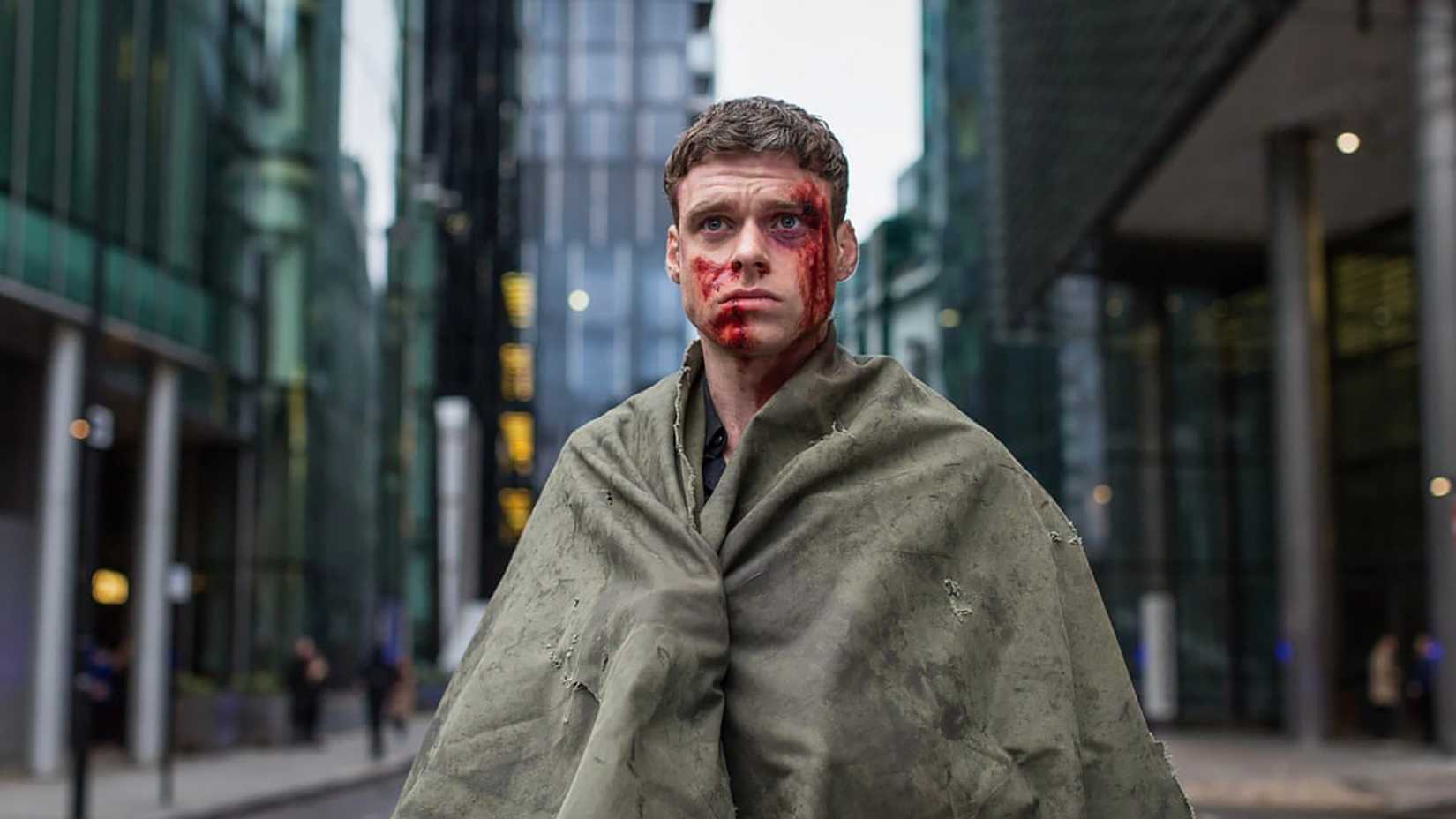 Richard Madden as David Budd with a bloody face, wrapped in a blanket in the middle of the street, in Bodyguard.