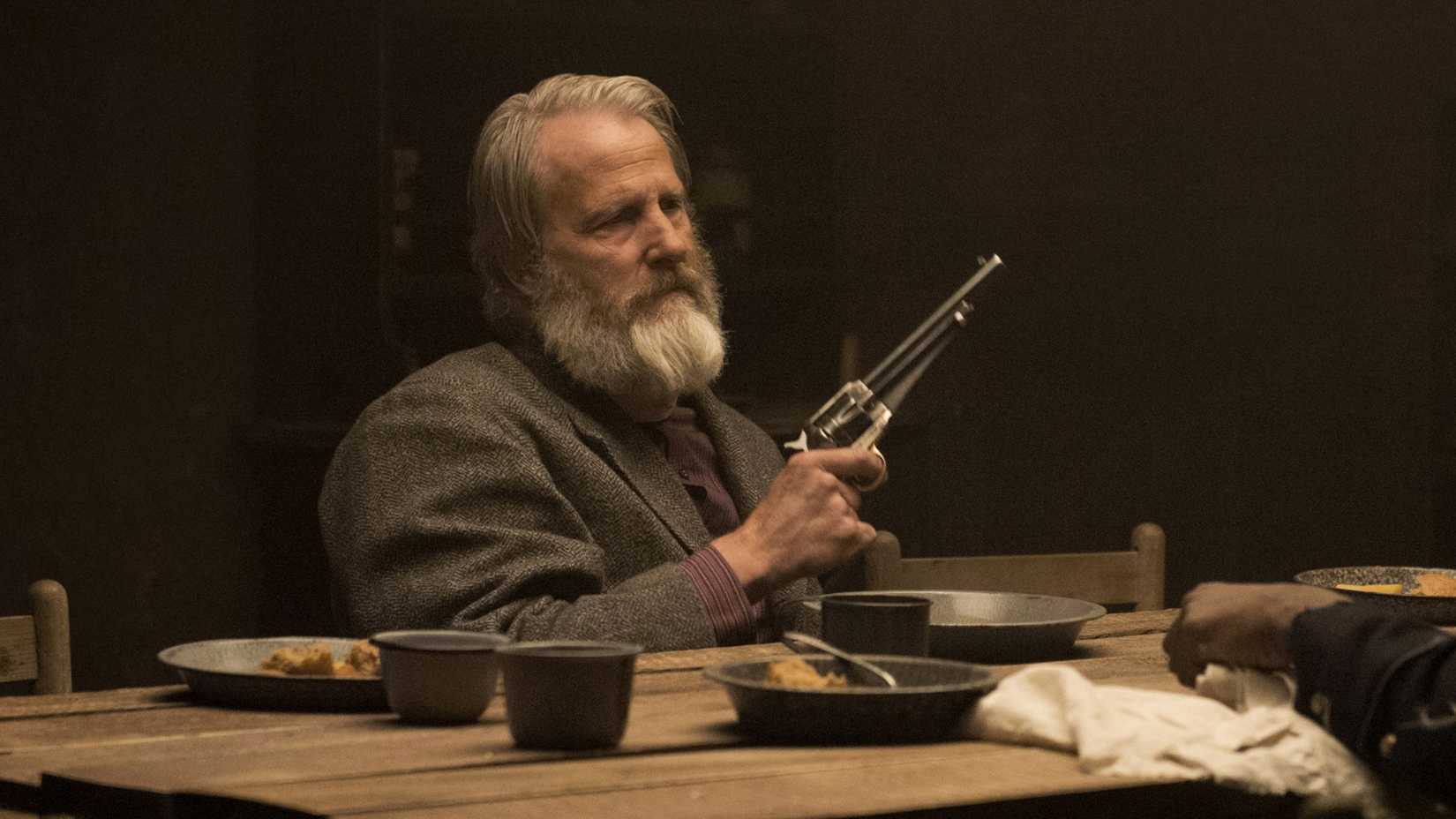 Jeff Daniels in Godless sitting down holding a gun.