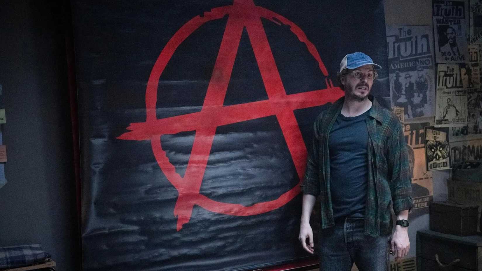 Elton stands by an anarchy mural in The Running Man