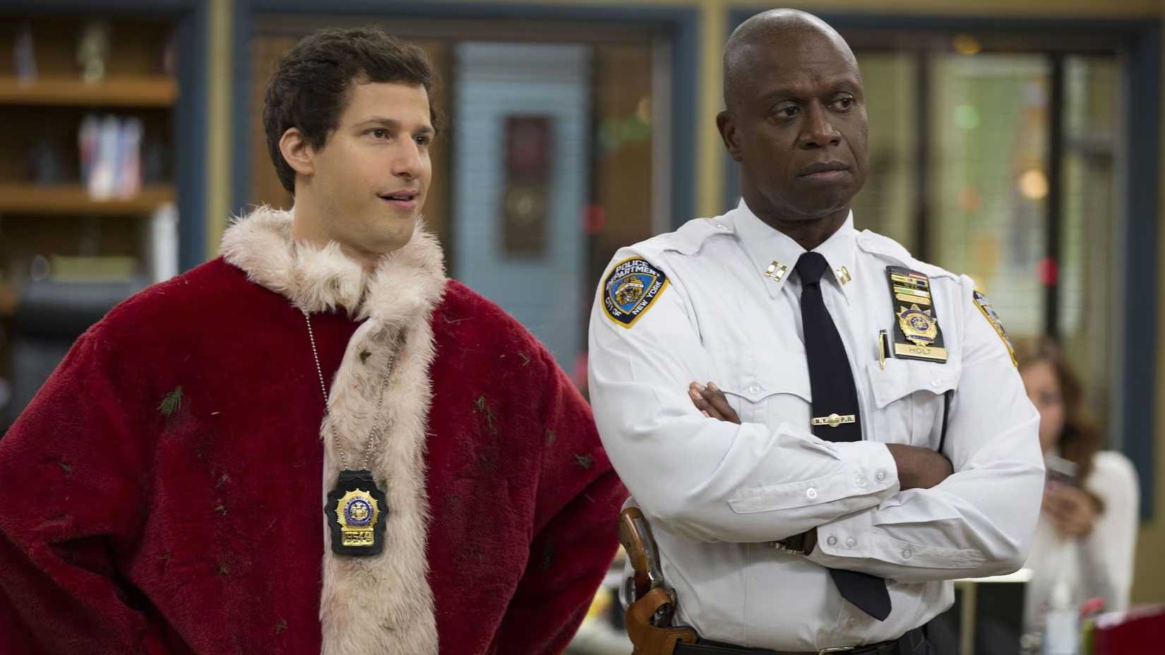Holt and Jake, who is dressed as Santa, standing together in the precinct in Brooklyn Nine-Nine.