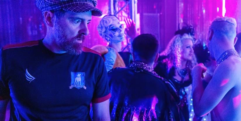 Coach Beard looking stunned in a nightclub while surrounded by party goers in Ted Lasso.