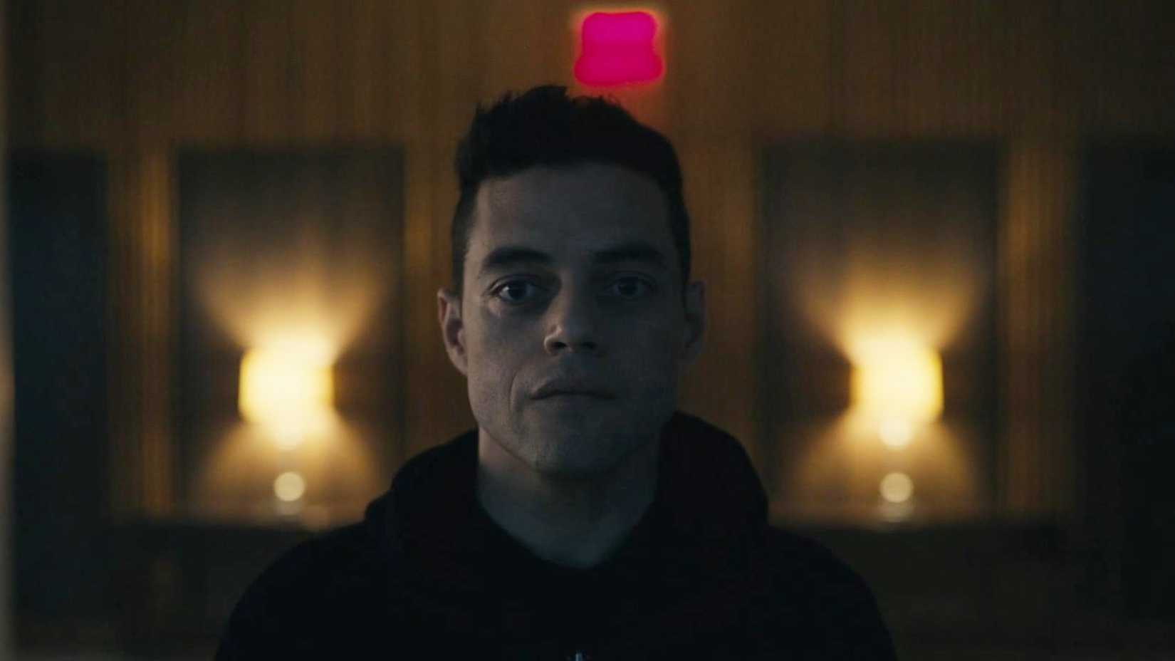 Rami Malek as Elliot staring straight ahead while sitting in a hotel room in Mr. Robot.