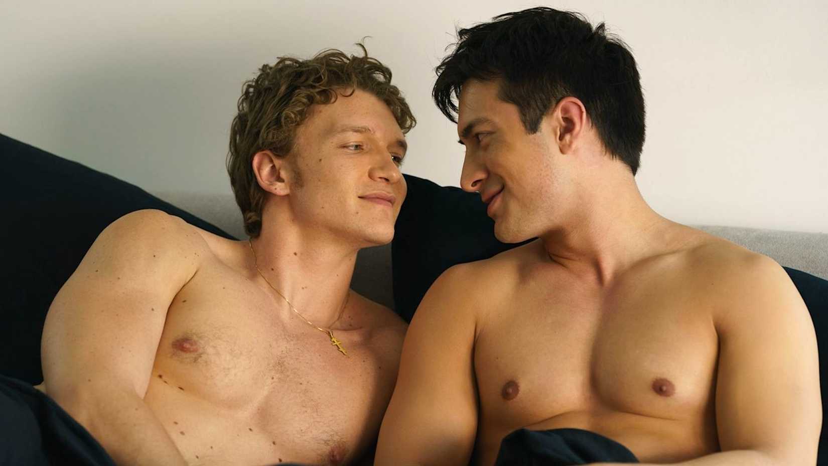 Connor Storrie and Hudson Williams smiling in bed in 'Heated Rivalry'