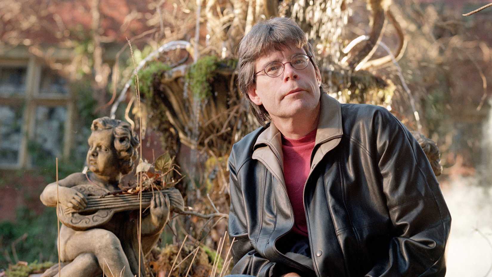 Stephen King sitting next to a statue in a behind the scenes photo on the set of Rose Red.