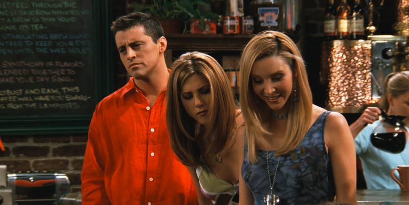 Rachel and Joey peering over as Phoebe shows a photo of her parents to everyone in Friends.