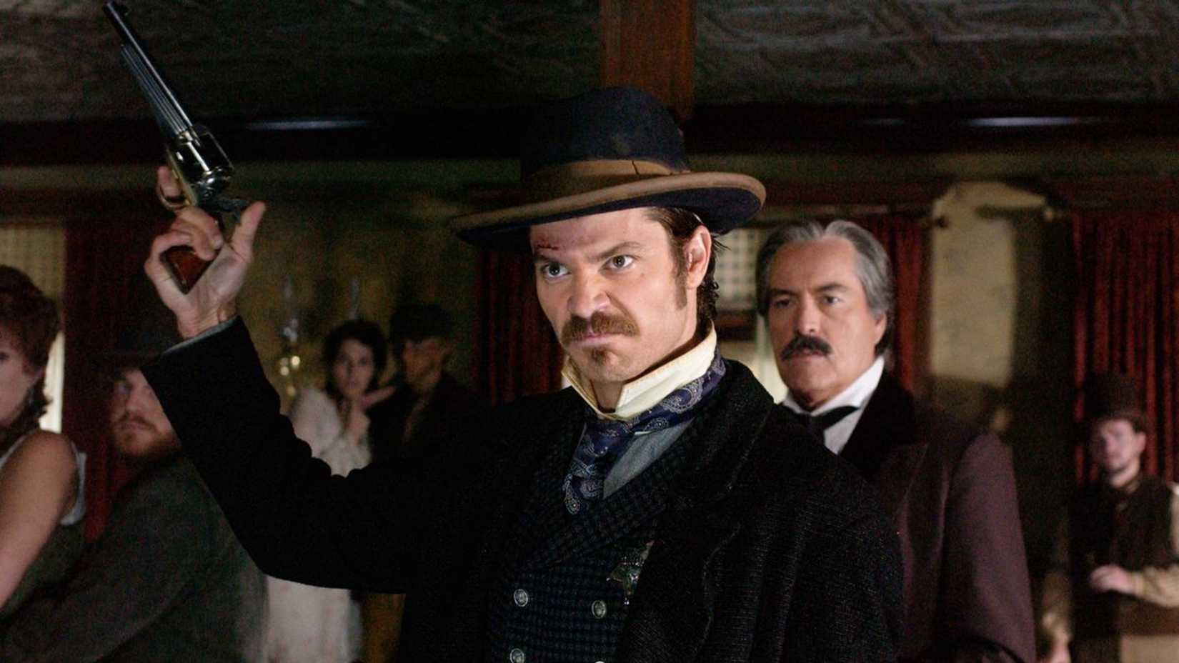 Seth aims a gun at the ceiling in Deadwood