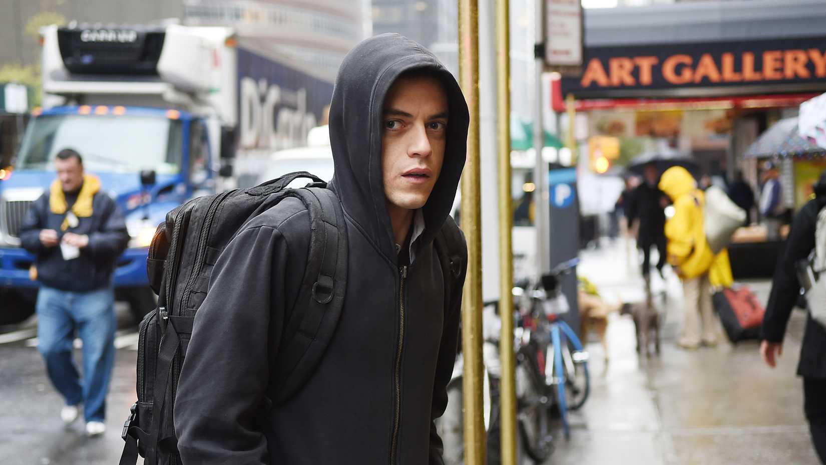 Elliot looking shifty as he stands in a busy street with his hood up in Mr. Robot.