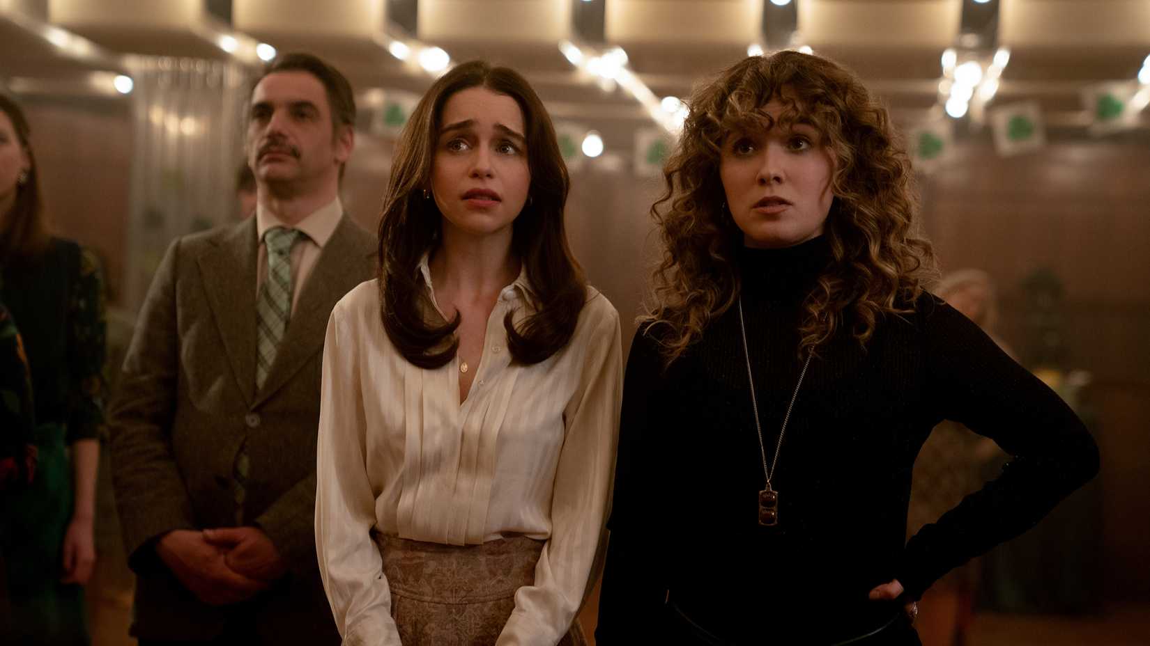 Bea and Twila looking concerned as they stand in a room surrounded by smartly dressed people in Ponies.