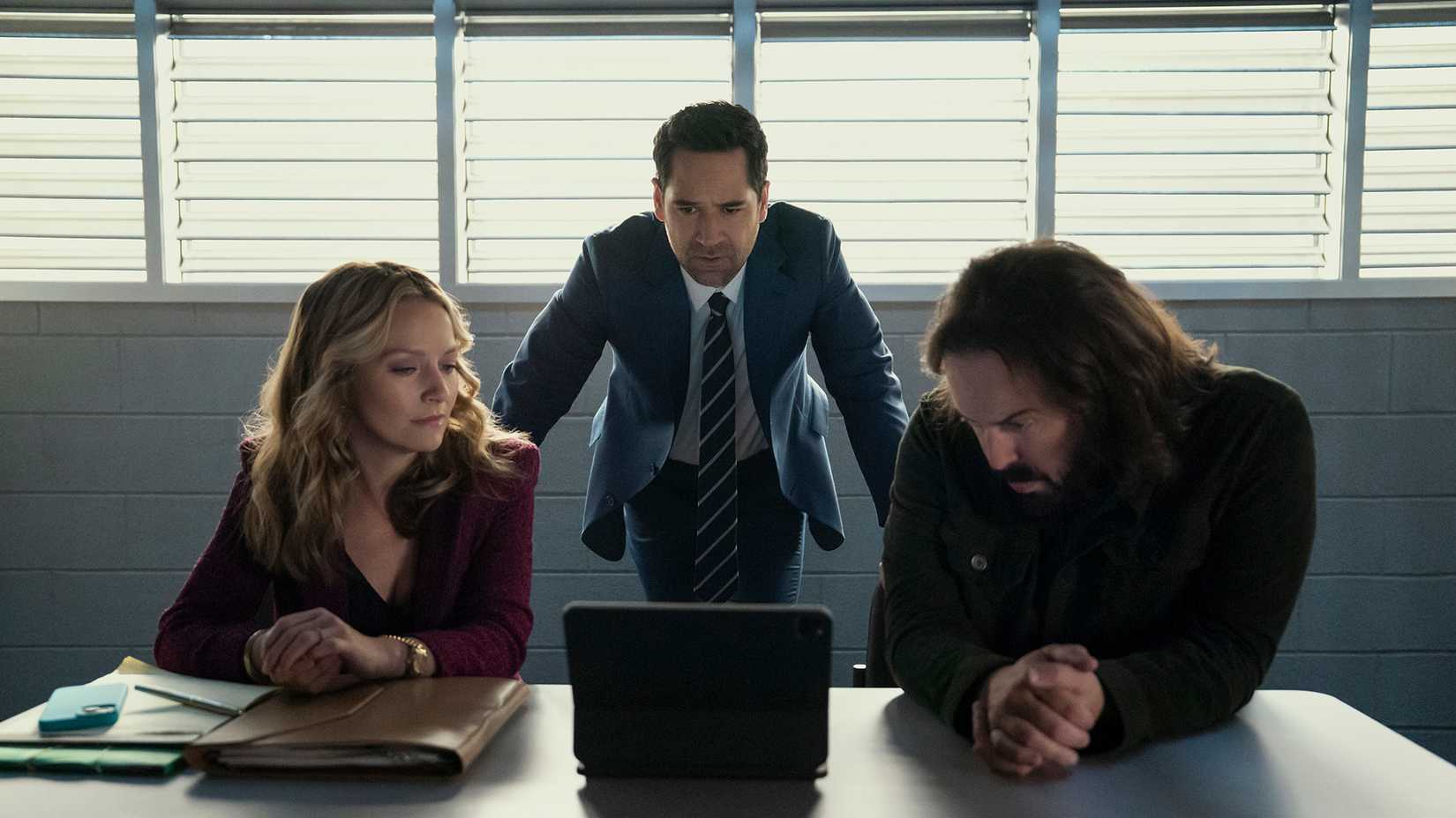 Mickey standing behind Lorna and Cisco looking at a laptop in The Lincoln Lawyer.