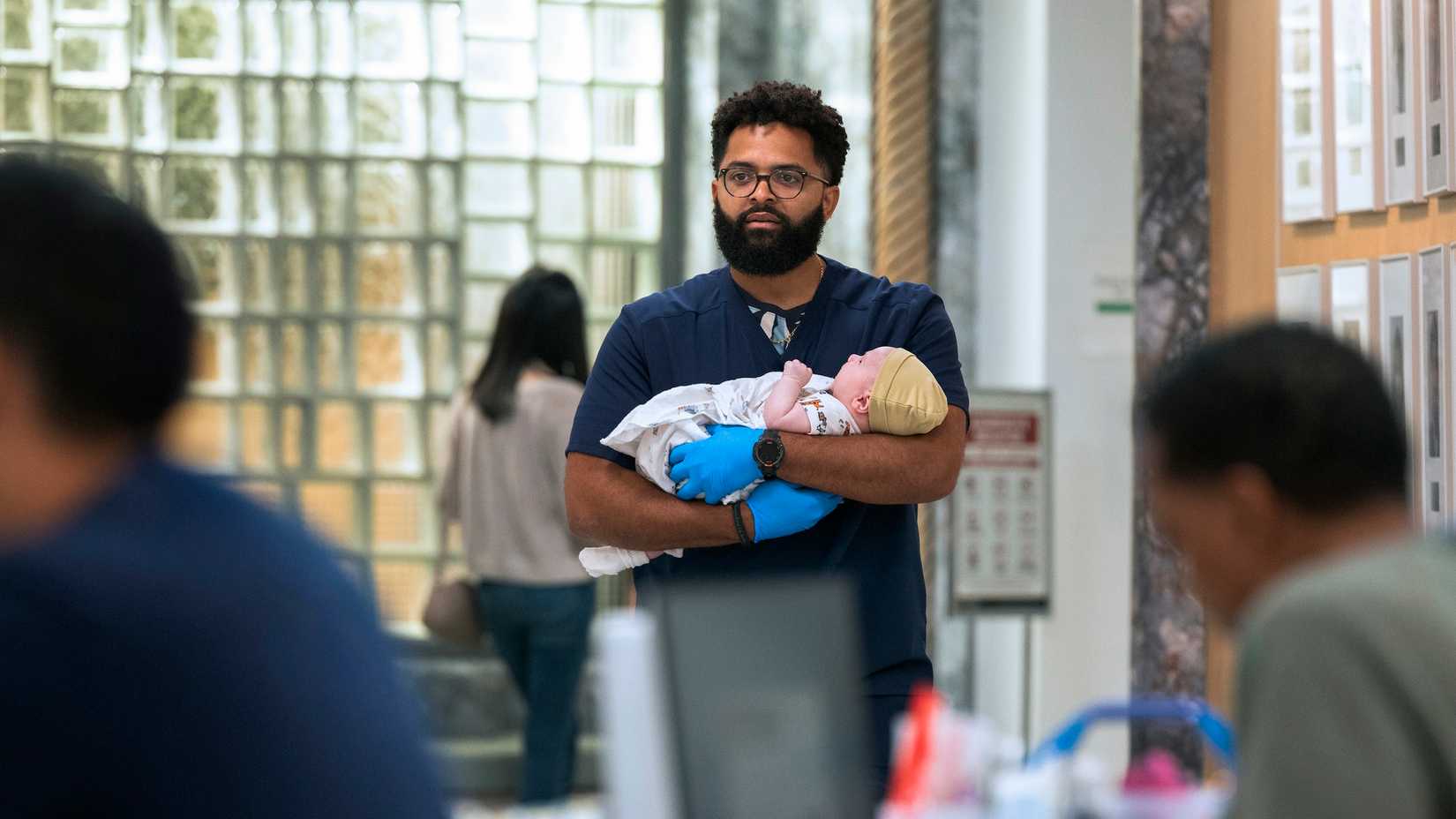 A male nurse holding a baby in The Pitt.