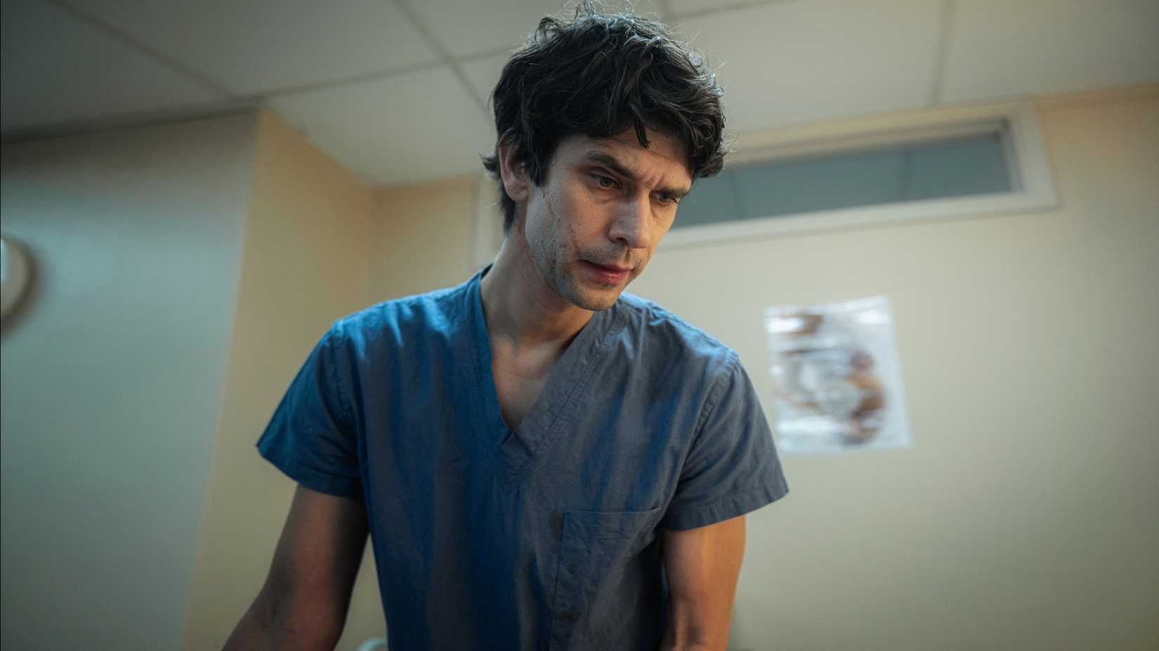 Ben Whishaw as Adam Kay with blood on his face, looking down at a patient, in This Is Going to Hurt.