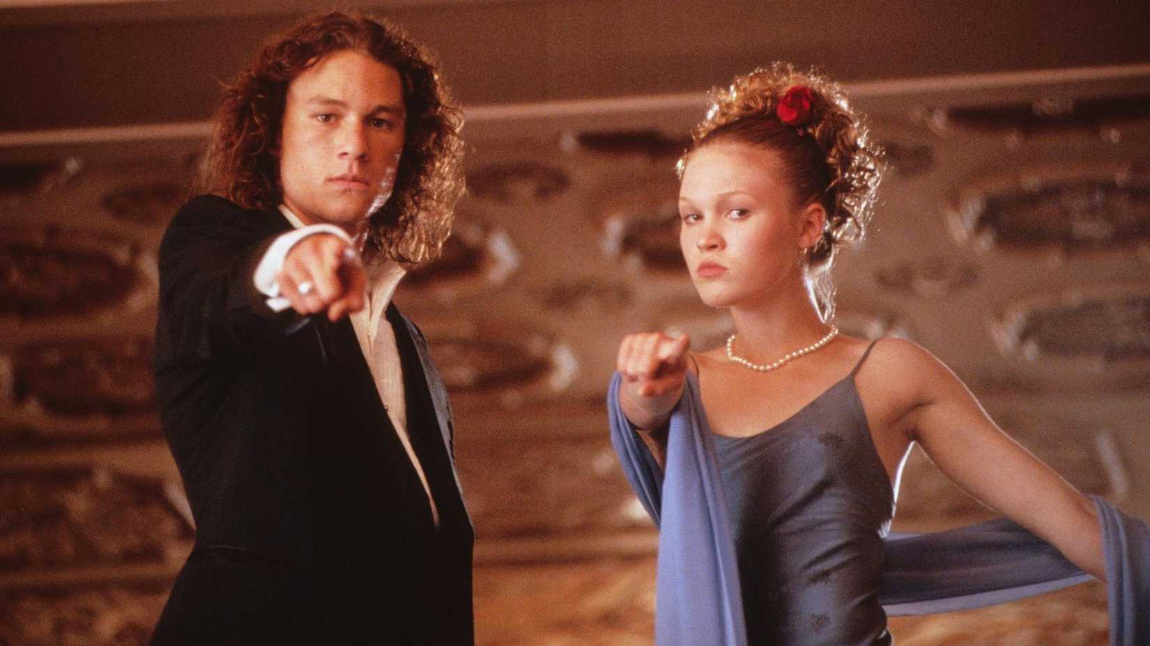 Heath Ledger as Patrick and Julia Stiles as Kat dressed up in nice clothing and pointing at the camera in 10 Things I Hate About You.