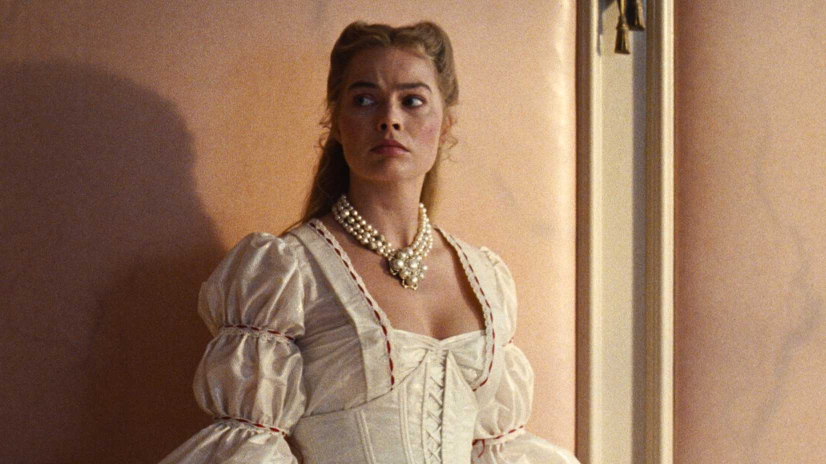 Margot Robbie as Cathy, leaning against the wall in her room, in Wuthering Heights.
