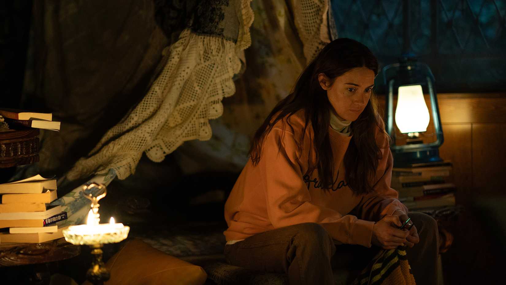 Annie sitting on a bed, looking pensive in Paradise Season 2.