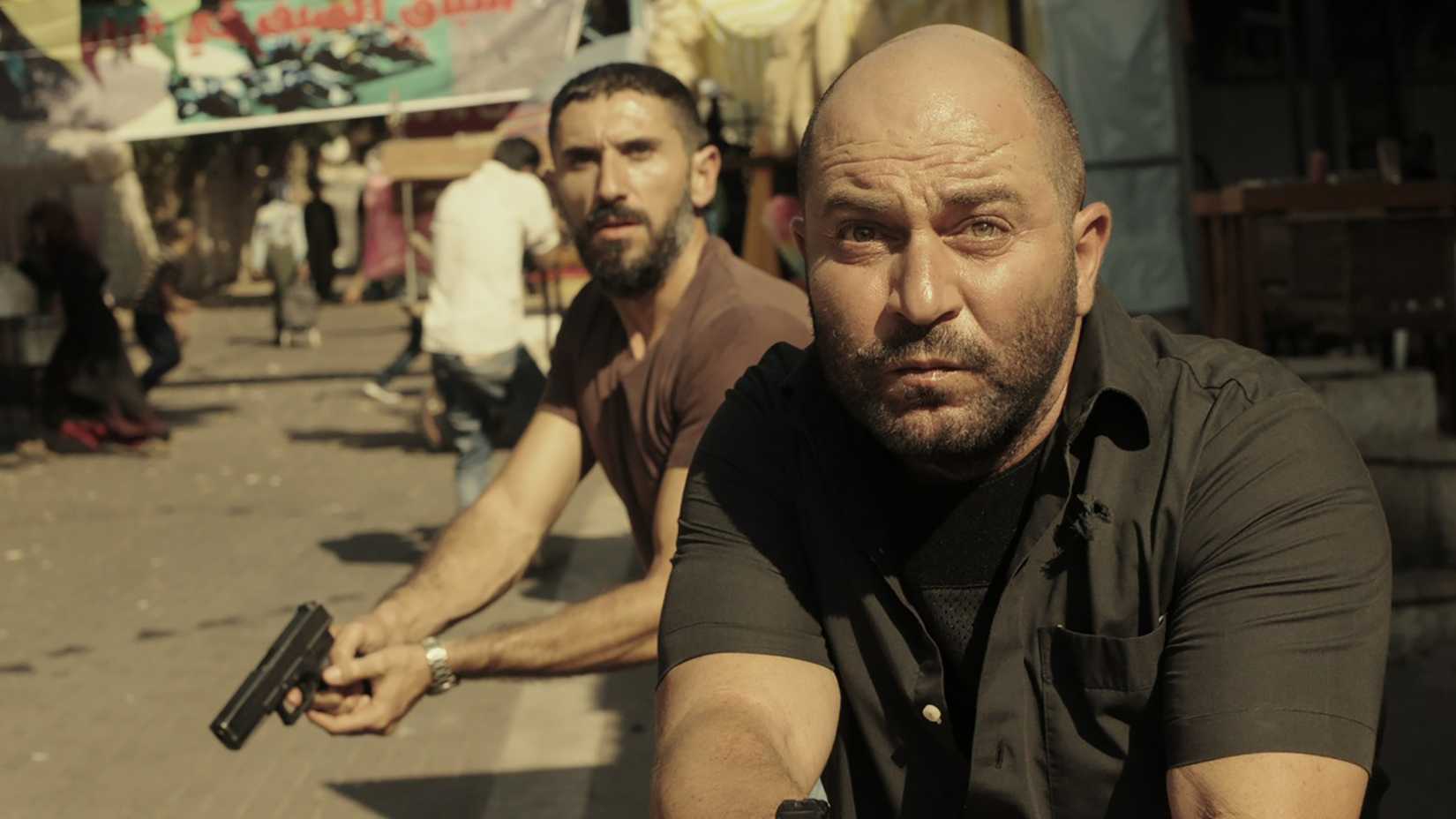 Two men holding guns and creeping around a corner in Fauda.