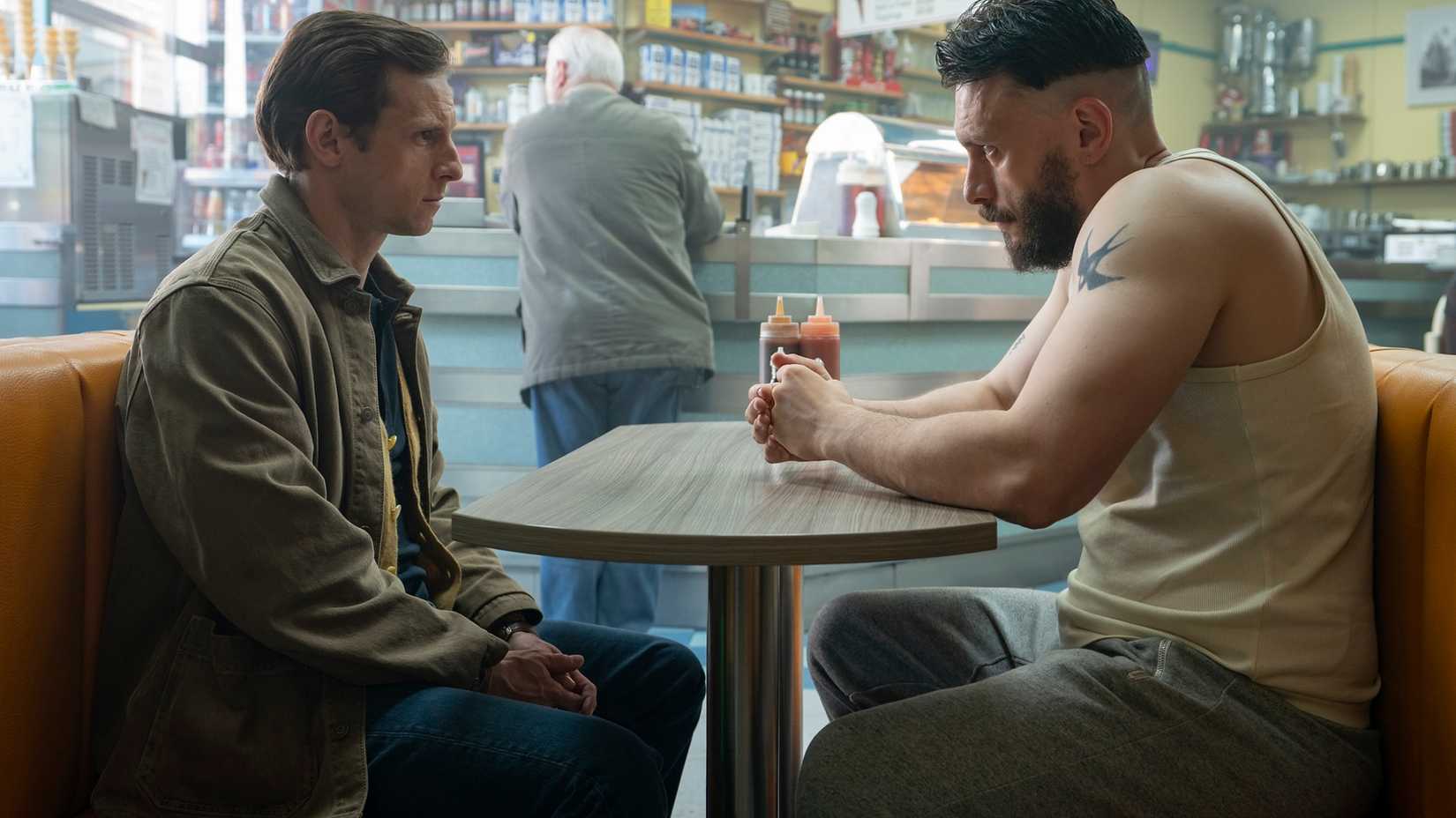 Niall and Ruben sitting across from each other in a diner, looking tense, in Half Man.