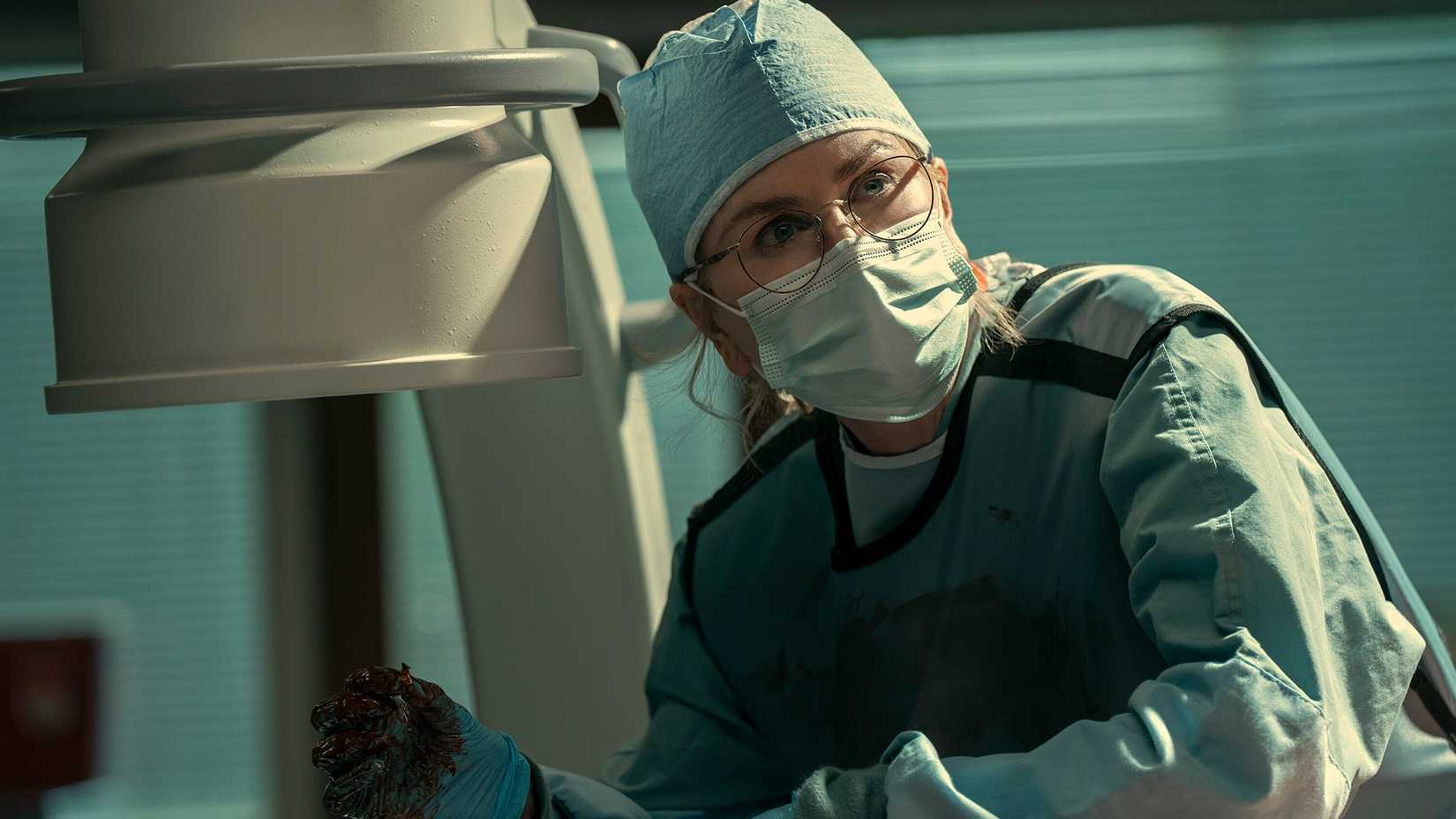 Dr. Kay wearing scrubs and a mask in Scarpetta.