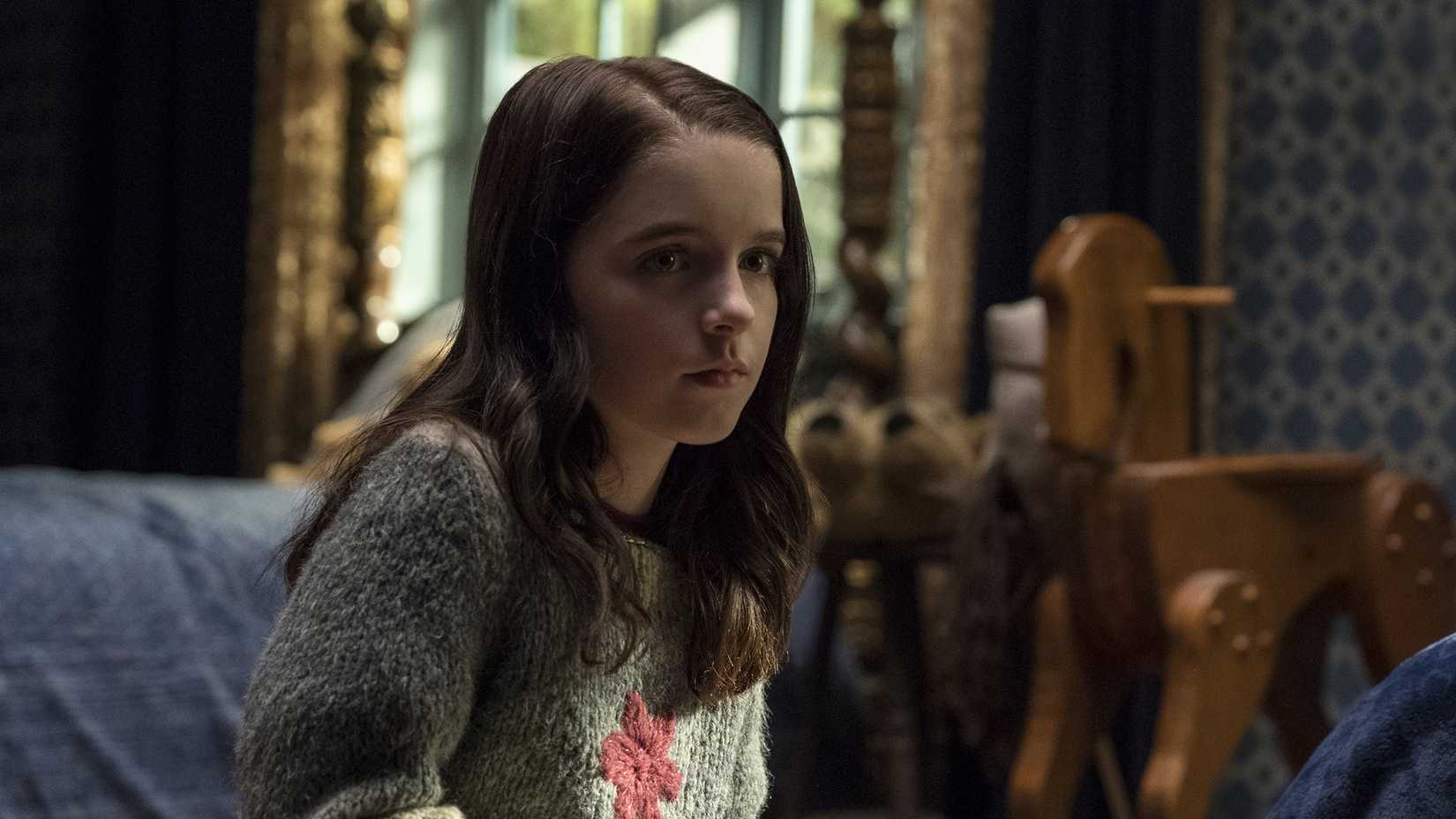 Mckenna Grace as Theo Crain looking unnerved as she sits in a bedroom and stares off at something in The Haunting of Hill House.