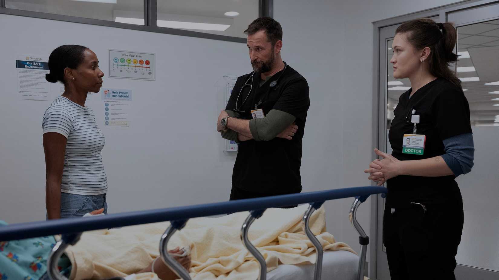 Robby arms folded talking to a patient's family member as Dr. Santos looks on in The Pitt.
