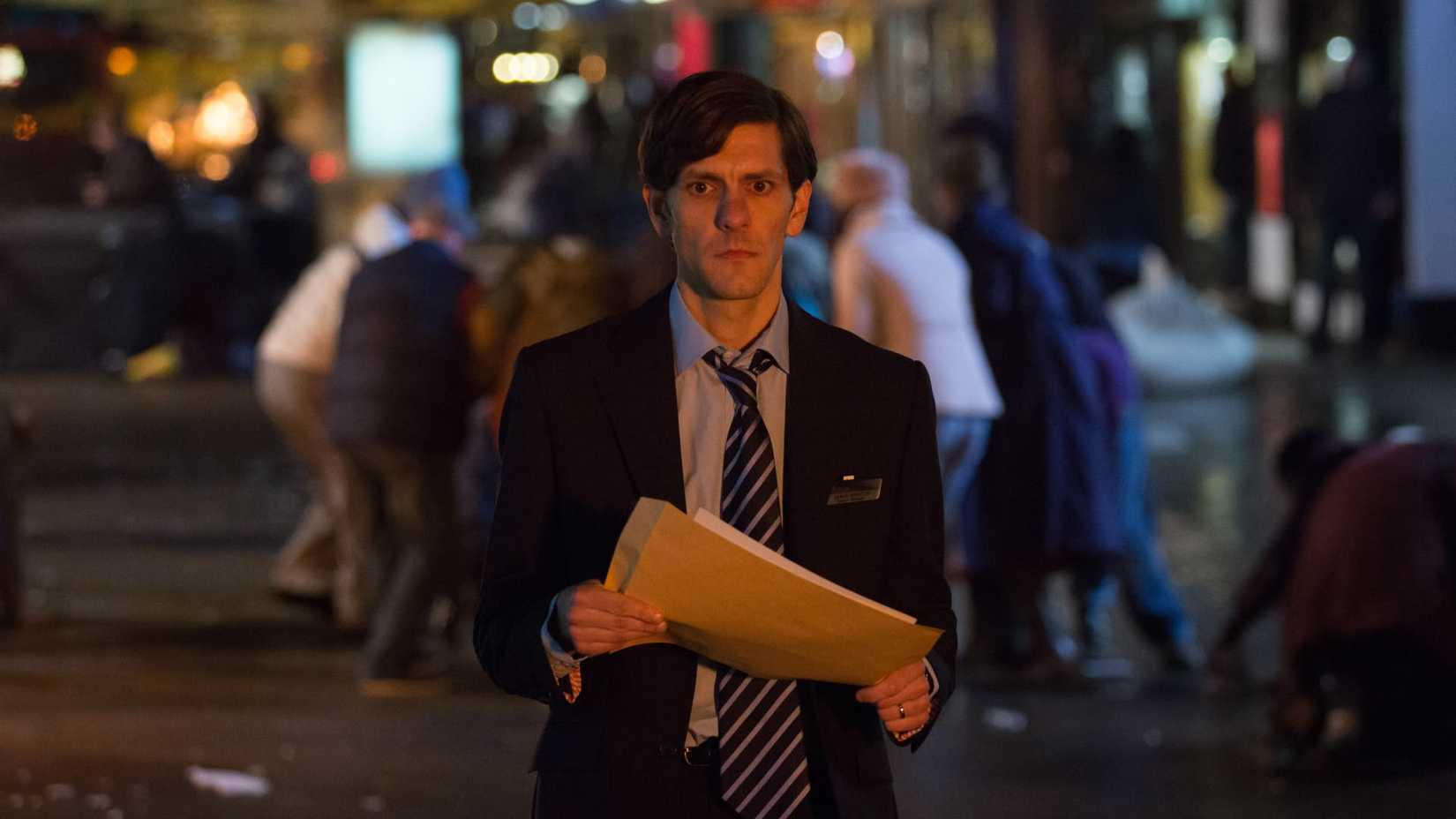Mathew Baynton as Jamie Winton looking defeated as he walks through a rioting street holding an envelope in You, Me and the Apocalypse.