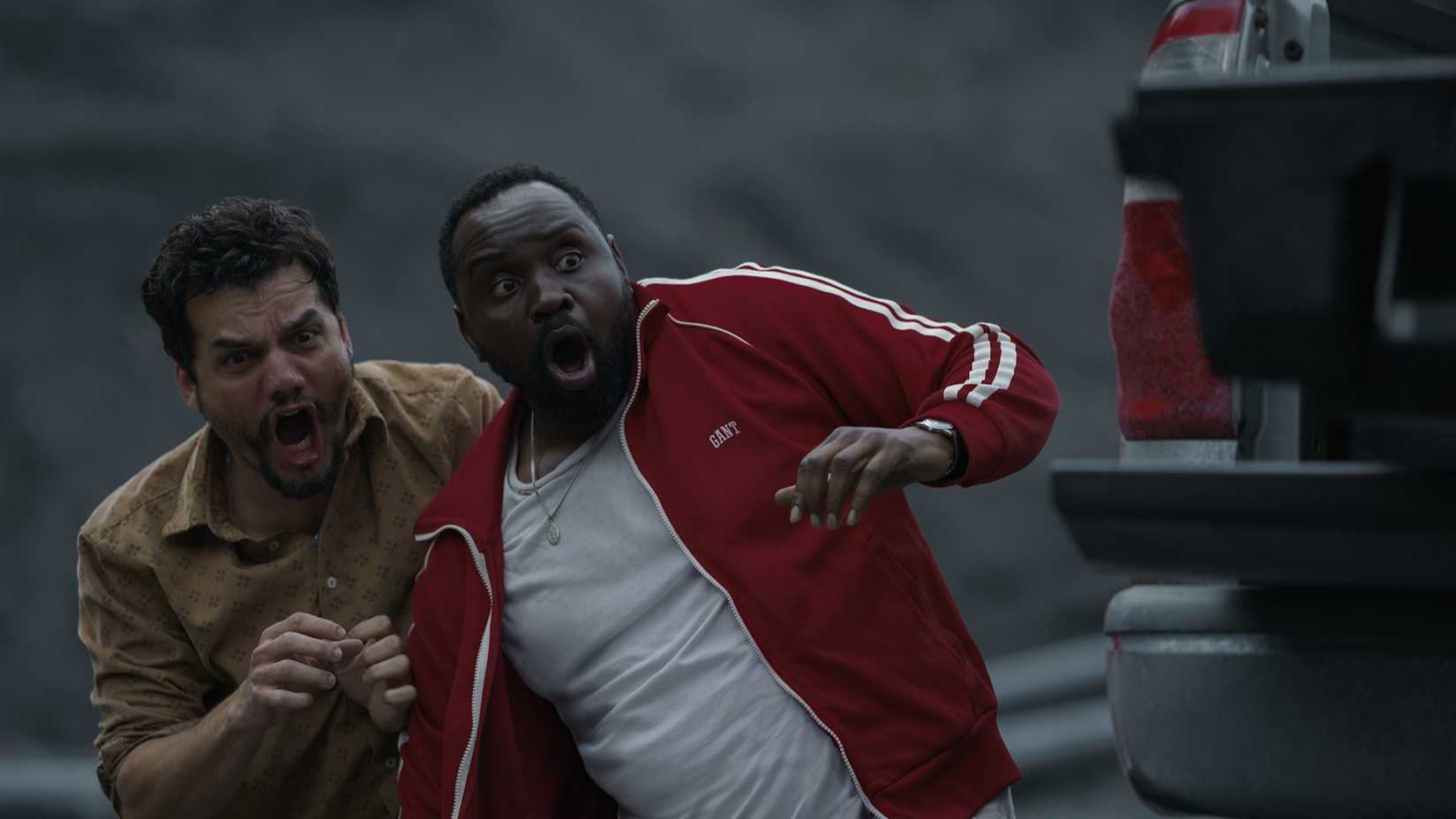 Brian Tyree Henry as Ray Driscoll and Wagner Moura as Manny Carvalho looking shocked as they stand by a car in Dope Thief.