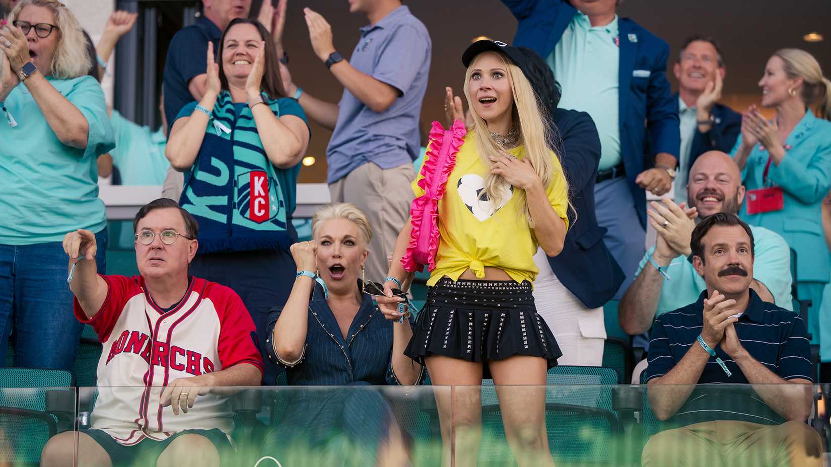 Leslie, Rebecca, Keeley, and Ted in the stands cheering on a team in Ted Lasso.