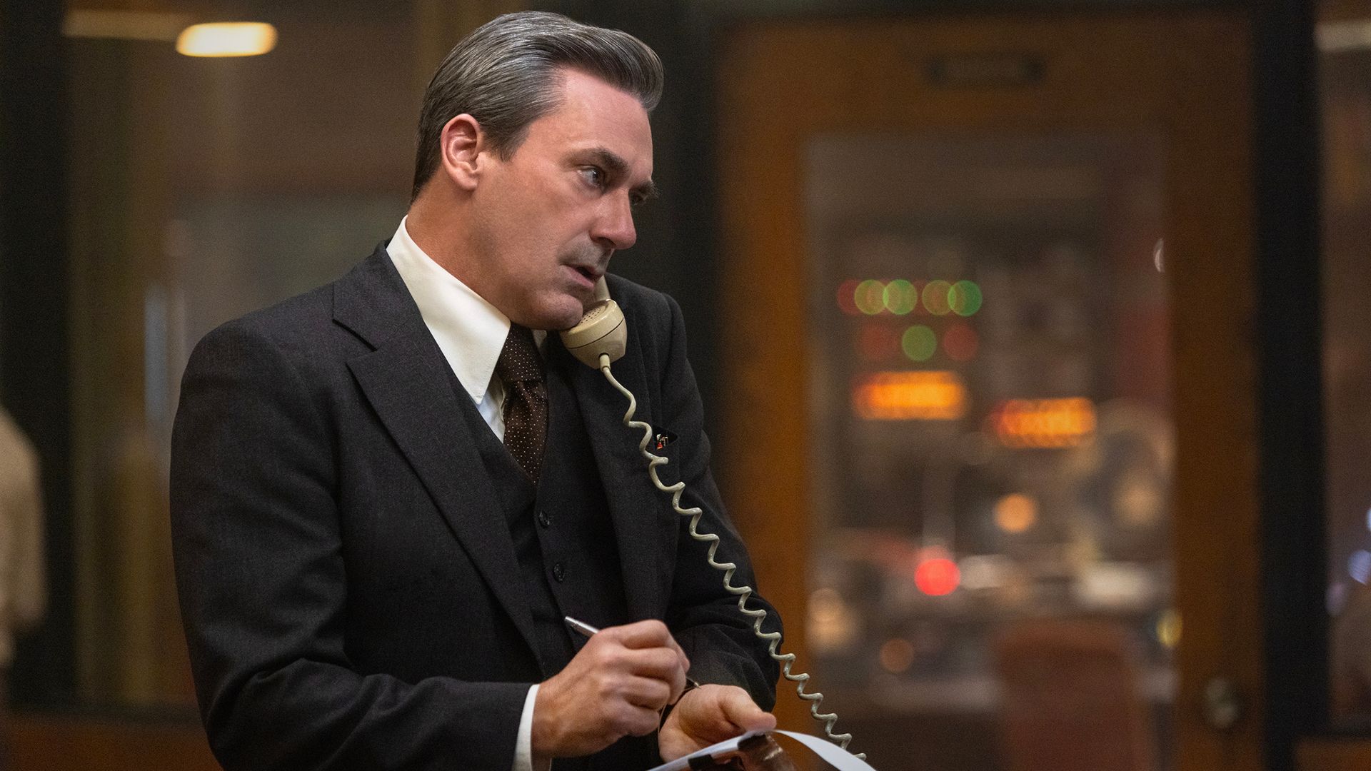 Fred in his office on the phone holding a notepad and pen in American Hostage.