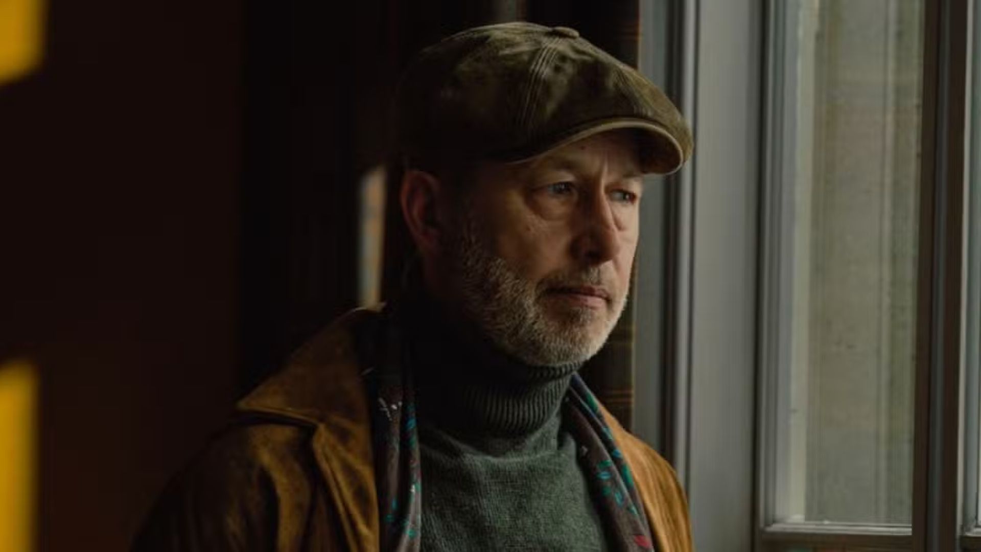 Brendan Harrigan wearing a flat cap and staring out of a window in MobLand.