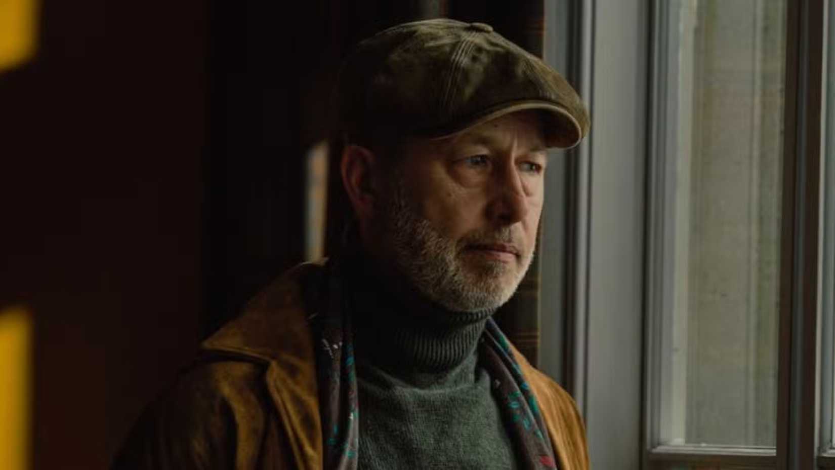 Brendan Harrigan wearing a flat cap and staring out of a window in MobLand.