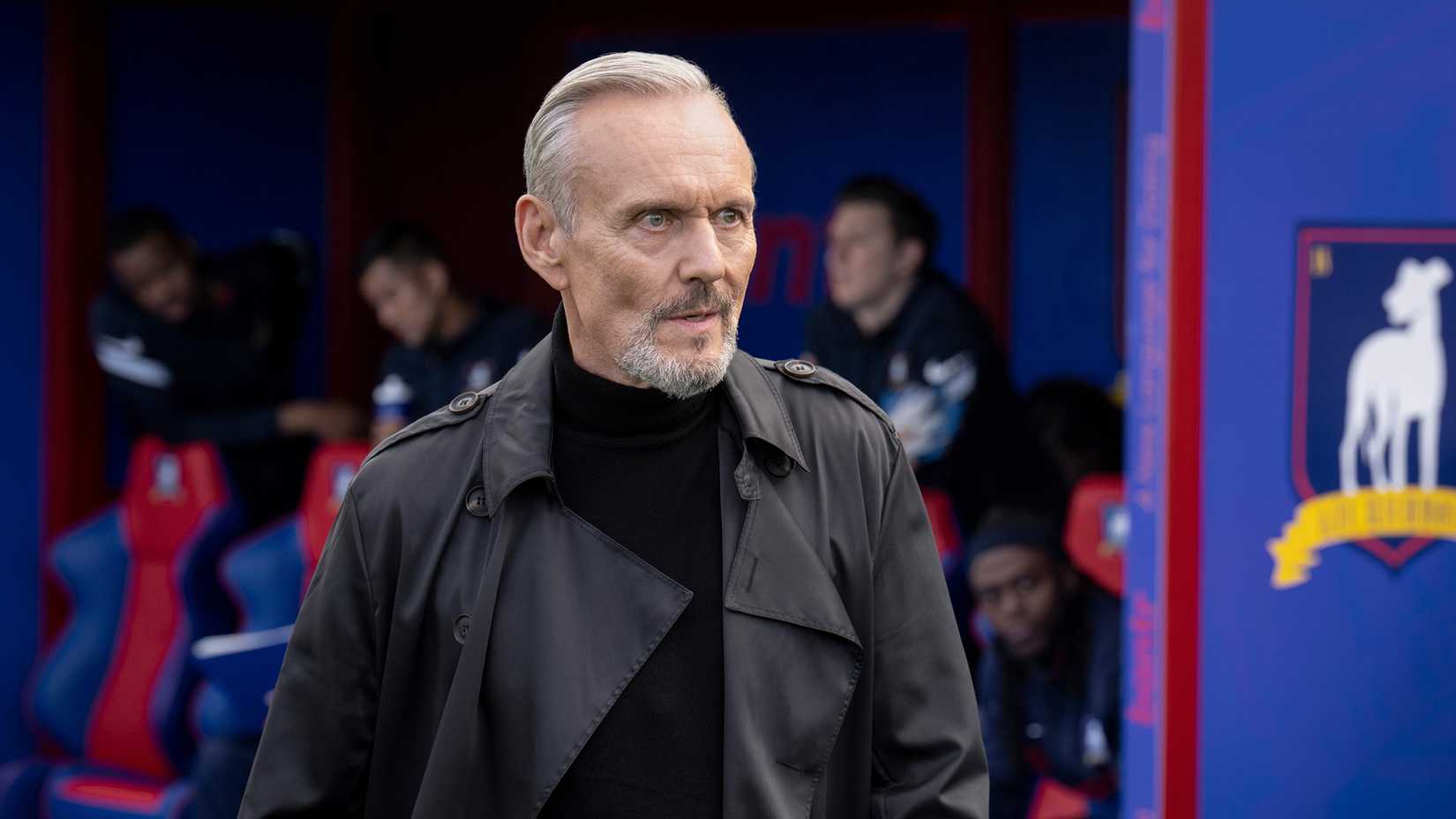 Anthony Head as Rupert Mannion standing on the sidelines of the pitch in Ted Lasso.