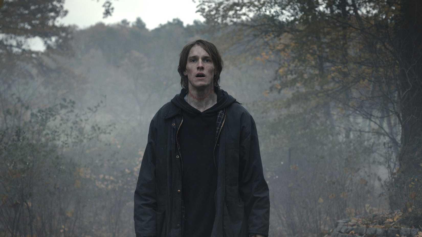 Jonas Kahnwald in the woods, staring ahead and looking exhaustd, in Dark.
