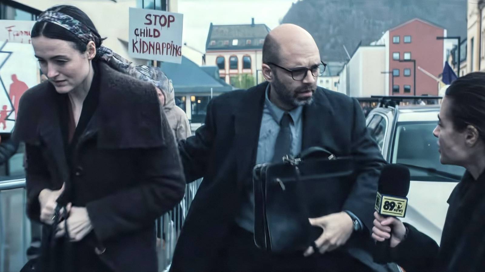Renate Reinsve And Sebastian Stan Walking Past A Crowd Of Protestors While Approached By A Reporter In Fjord